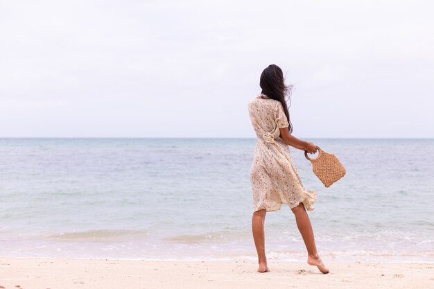 Retrato romántico de mujer con vestido largo en la playa en día nublado con viento.