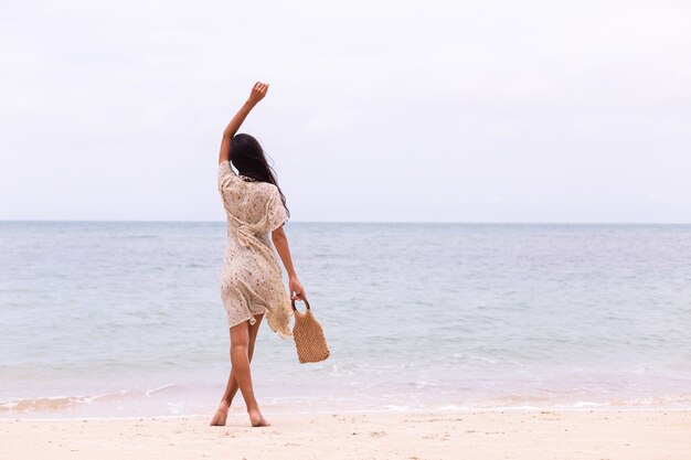 Retrato romántico de mujer con vestido largo en la playa en día nublado con viento.