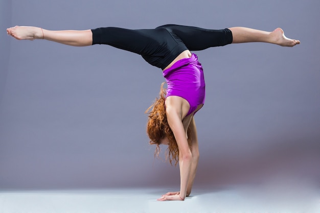 Retrato de ropa deportiva hermosa joven trabajando en fondo gris. Colocar chica deportiva haciendo yoga avanzado, pilates, fitness.