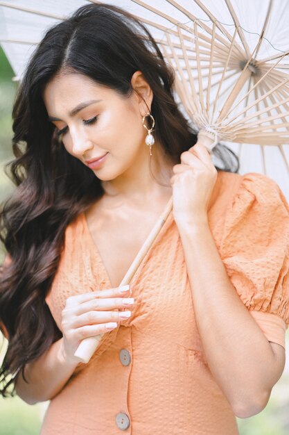 Retrato de la señora bonita en la naturaleza con paraguas en vestido naranja durante el día.