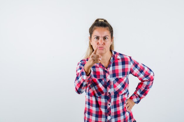 Retrato de señorita advirtiendo con el dedo en camisa a cuadros y mirando nervioso vista frontal