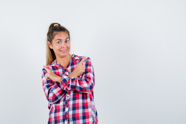 Retrato de señorita apuntando hacia afuera en camisa a cuadros y mirando jovial vista frontal