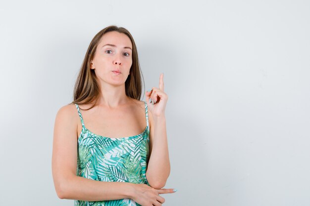 Retrato de señorita apuntando hacia arriba en blusa y mirando confiada vista frontal