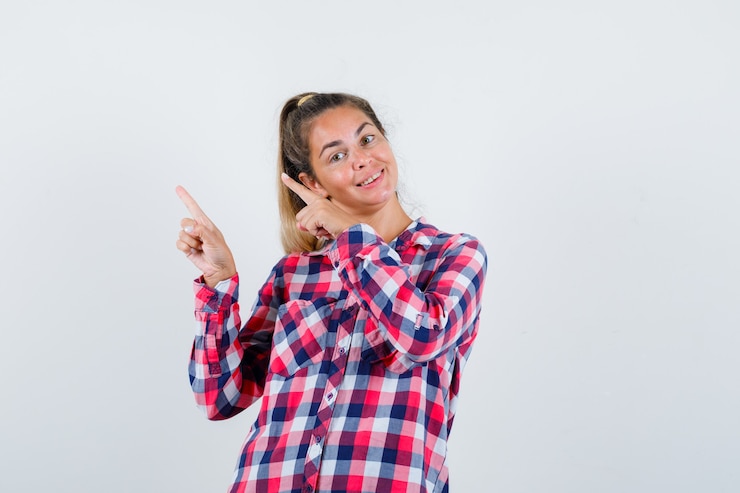 Foto gratuito retrato de señorita apuntando a la esquina superior izquierda en camisa a cuadros y mirando alegre vista frontal