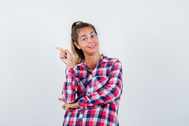 Retrato de señorita apuntando hacia el lado izquierdo en camisa a cuadros y mirando alegre vista frontal