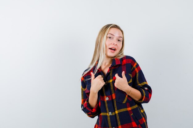 Retrato de señorita apuntando a sí misma en camisa a cuadros y mirando orgullosa vista frontal