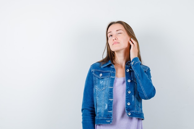 Retrato de señorita escuchando una conversación privada en camiseta, chaqueta y mirando curiosa vista frontal