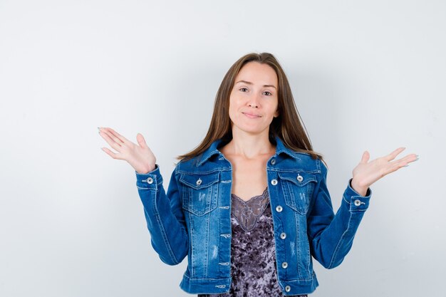 Retrato de señorita fingiendo sostener algo en blusa, chaqueta vaquera y mirando alegre vista frontal