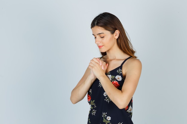 Retrato de señorita juntando las manos en gesto de oración en blusa y mirando pacífica vista frontal