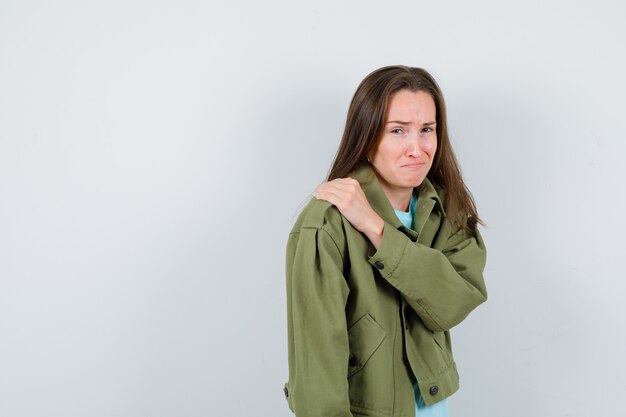 Retrato de señorita con la mano en el hombro en camiseta, chaqueta y mirando ofendido vista frontal