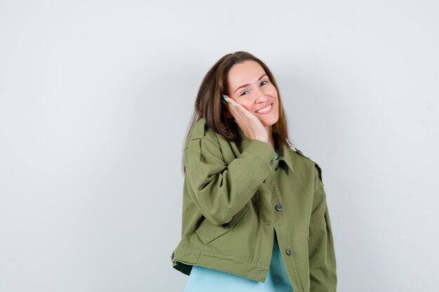 Retrato de señorita con la mano en la mejilla en camiseta, chaqueta y mirando hermosa vista frontal