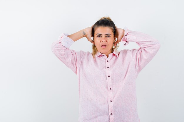 Retrato de señorita manteniendo las manos detrás de la cabeza en camisa rosa y mirando sorprendido vista frontal