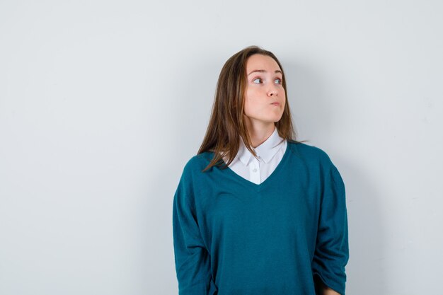 Retrato de señorita mirando a otro lado, haciendo muecas en camisa blanca, suéter y mirando enfocada vista frontal