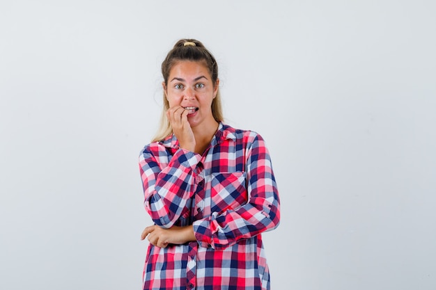 Retrato de señorita mordiéndose las uñas en camisa a cuadros y mirando preocupado vista frontal