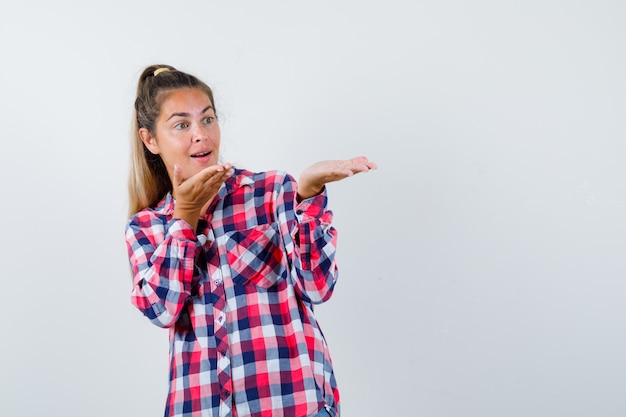 Retrato de señorita mostrando algo en camisa a cuadros y mirando asombrado vista frontal