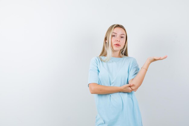 Retrato de señorita mostrando algo en camiseta y mirando confiado aislado