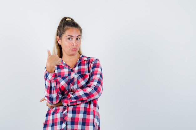 Retrato de señorita mostrando el pulgar hacia arriba en camisa a cuadros y mirando confiada vista frontal