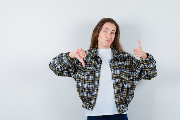 Foto gratuita retrato de señorita mostrando los pulgares hacia arriba y hacia abajo en camiseta, chaqueta y mirando vacilante vista frontal