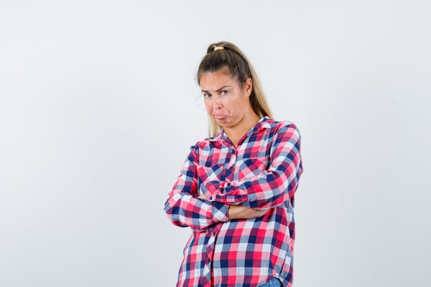 Retrato de señorita de pie con los brazos cruzados en camisa a cuadros y mirando dudosa vista frontal