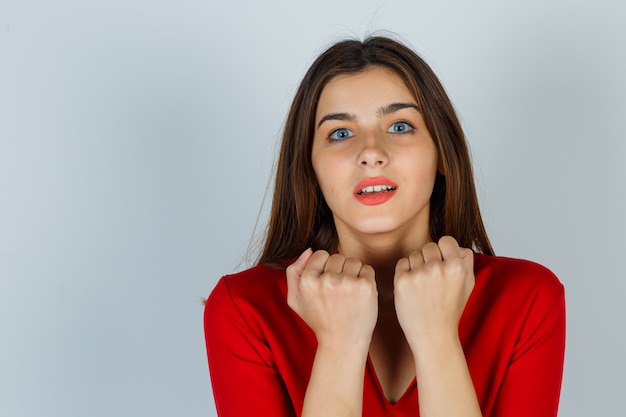 Retrato de señorita de pie en pose asustada en blusa roja y mirando asustado