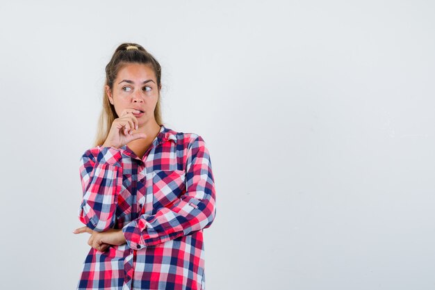 Retrato de señorita de pie en pose de pensamiento en camisa a cuadros y mirando enfocado vista frontal