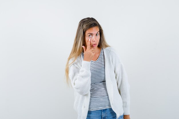 Retrato de señorita tirando hacia abajo de su párpado en camiseta, chaqueta y mirando seria vista frontal