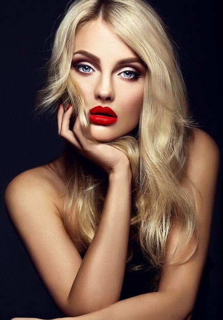 Retrato sensual glamour de hermosa mujer rubia modelo dama con maquillaje brillante y labios rojos, con cabello rizado saludable sobre fondo negro