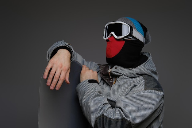 Foto gratuita retrato de un snowboarder con equipo de protección completo para snowboard extremo posando con snowboard en un estudio, aislado en un fondo oscuro.