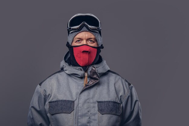 Retrato de un snowboarder vestido con un equipo de protección completo para el snowboard extremo posando en un estudio. Aislado en el fondo gris.