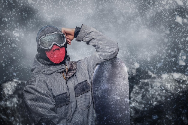 Retrato de un snowboarder vestido con un equipo de protección completo para el snowboard extremo posando con snowboard contra el fondo de las montañas
