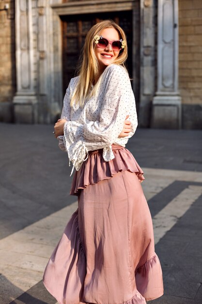 Retrato soleado de lujo de moda de mujer rubia posando en la calle con blusa y falda larga de seda