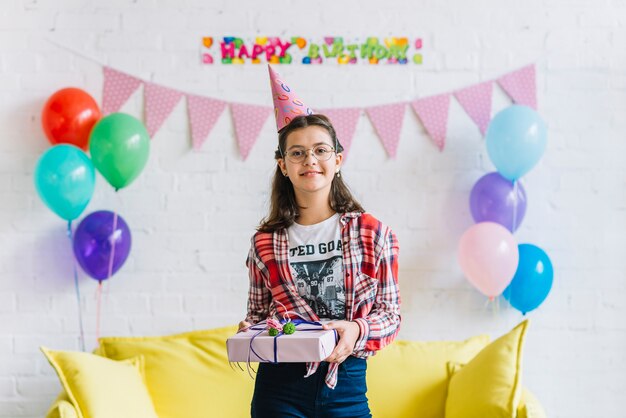 Retrato del sombrero del partido de la muchacha que lleva feliz que sostiene el regalo de cumpleaños