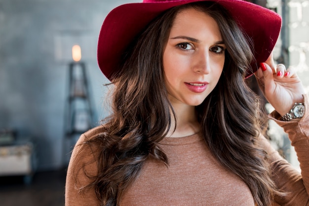 Retrato de un sombrero que lleva hermoso de la mujer joven que mira la cámara