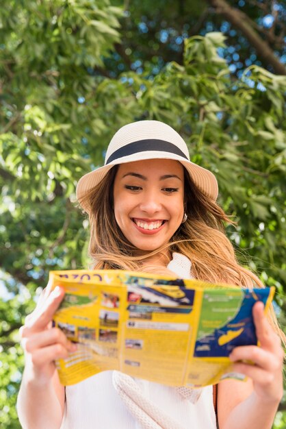 Retrato del sombrero que lleva sonriente de la mujer joven sobre el mapa principal de la lectura