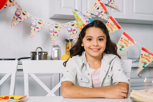 Retrato de un sombrero sonriente del partido de la muchacha del cumpleaños que lleva en la cabeza que mira la cámara