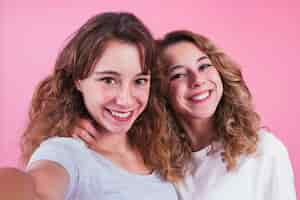 Foto gratuita retrato de sonreír a dos hermanas contra el fondo rosado