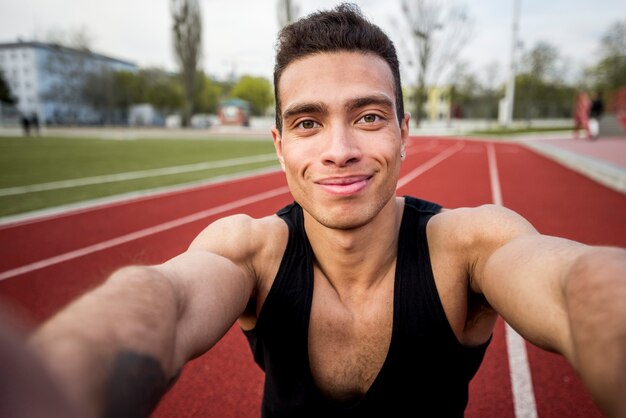 Retrato de un sonriente atleta masculino en la pista de carreras tomando selfie