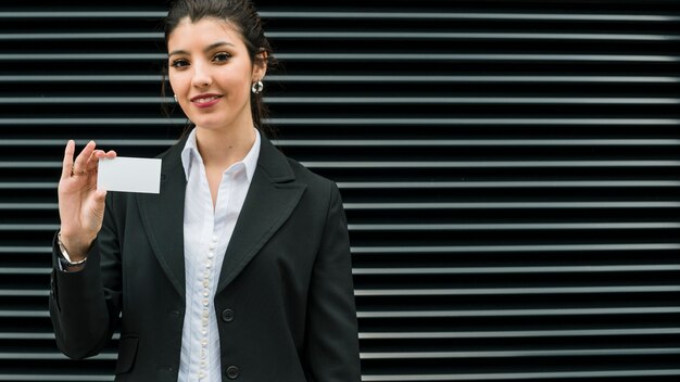 Retrato sonriente confiado de una empresaria joven sonriente que muestra la tarjeta de visita blanca