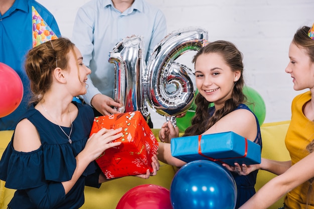 Retrato sonriente de la cumpleañera con el globo de la hoja número 16 y regalos