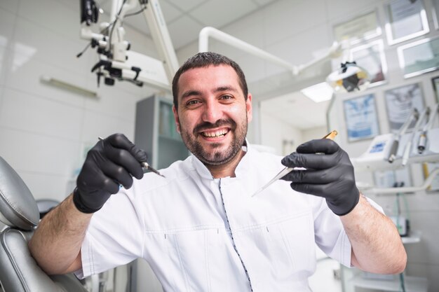 Retrato de sonriente dentista masculino con herramientas dentales