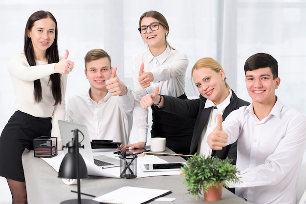 Retrato sonriente de los empresarios que muestran el pulgar encima de la muestra