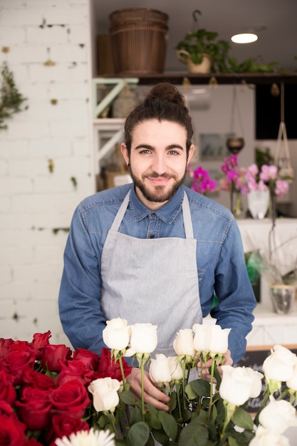 Retrato sonriente de un florista de sexo masculino joven que sostiene las flores blancas disponibles