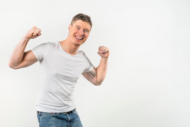 Retrato sonriente de un hombre joven que dobla sus músculos contra el fondo blanco