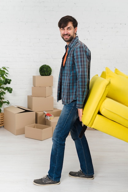 Foto gratuita retrato sonriente de un hombre joven que levanta el sofá amarillo en casa nueva