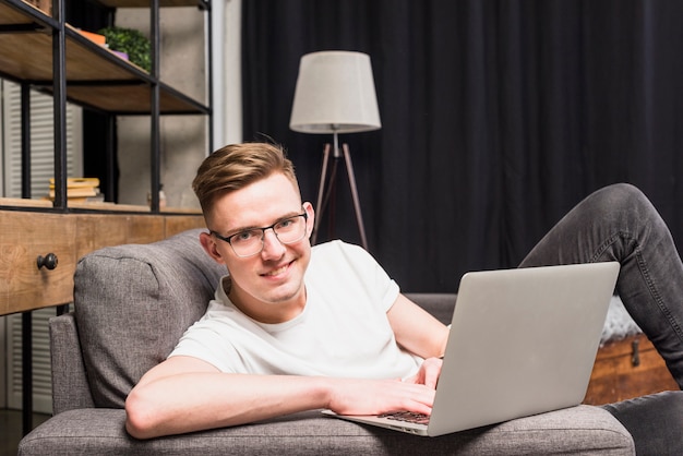 Retrato sonriente de un hombre joven que usa la computadora portátil que mira a la cámara