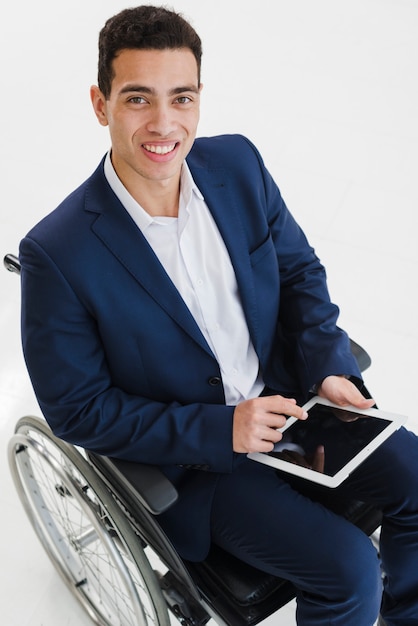 Foto gratuita retrato sonriente de un hombre joven sentado en silla de ruedas usando tableta digital