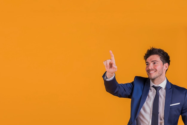 Retrato sonriente de un hombre de negocios joven que señala su dedo en algo en un fondo anaranjado