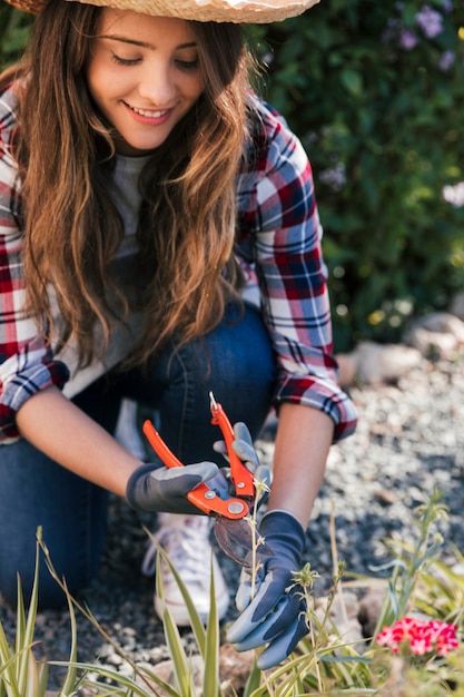 Foto gratuita retrato sonriente de un jardinero de sexo femenino joven que corta la ramita con esquileos