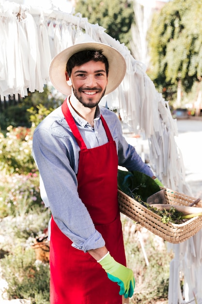 Retrato sonriente de un jardinero de sexo masculino en el delantal rojo que mira la cámara