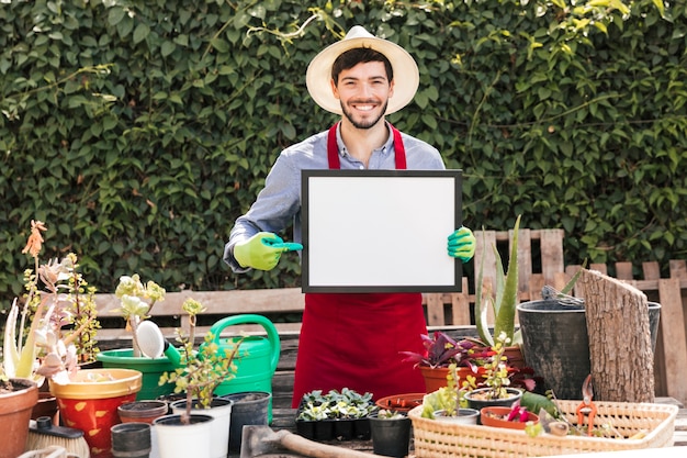 Retrato sonriente de un jardinero de sexo masculino que señala el dedo en marco blanco en blanco